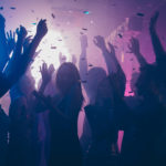 Close up photo of many party people dancing purple lights confetti flying everywhere nightclub event hands raised up wear shiny clothes