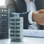 housing development and investment business – businessmen handshake after agreement of apartment building construction. banner copy space