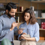 Indian manager holding digital tablet having discussion with latin employee.