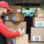 Happy courier with truck signing delivery of cardboard box on ta