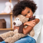 Depressed african american girl with autism hugging teddy bear w