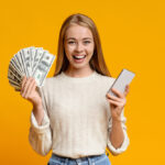 Happy teen girl showing holding smartphone and bunch of money