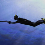 Diver pointing his speargun to the target fish under deep sea 3d